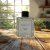 Difusor de ambiente Olibano 240 ml da marca Exalass em uma mesa de madeira com plantas ao fundo.