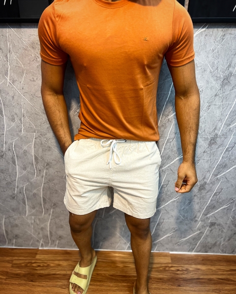 Modelo vestindo shorts de linho premium na cor Areia, com camiseta Telha e chinelos.