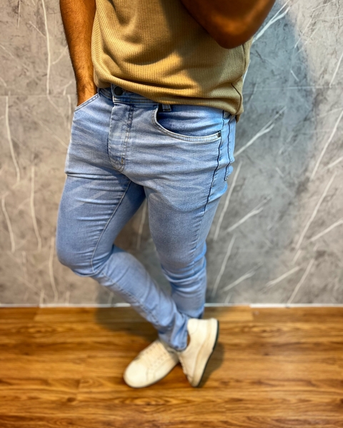 Calça jeans tradicional premium em tom claro, vista lateral, com modelo masculino usando camisa bege e tênis branco.