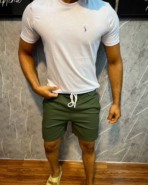 Modelo vestindo shorts de linho premium na cor Verde, com camiseta branca e chinelos.