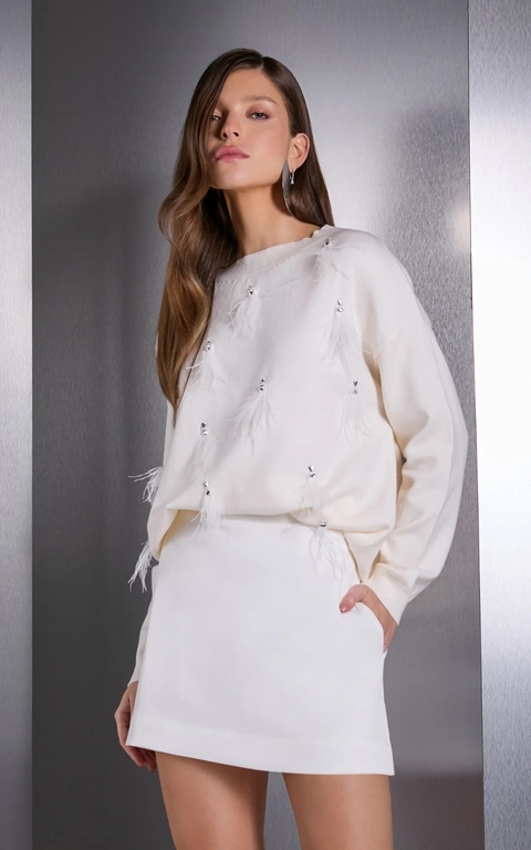 Modelo usando uma blusa de tricô branca com bordado de plumas e detalhes em strass.