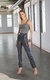 A imagem apresenta uma modelo em um ambiente de estilo industrial, vestindo uma calça reta que se destaca por sua superfície coberta de paetês brilhantes em tons de cinza e prata, criando um efeito "glow". 