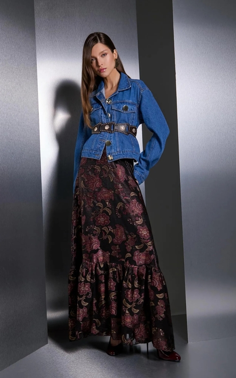 A modelo está com uma jaqueta jeans de comprimento cropped, terminando na altura da cintura. A jaqueta tem um tom de azul jeans clássico.