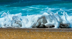Espuma do mar explode na areia da Praia do Moçambique, em Floripa. Foto macro capta a força e a beleza natural com detalhes impressionantes.