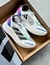 Zapatillas Adidas Adizero Boston en una caja, con diseño moderno en tonos blancos y detalles de colores vivos.