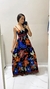 Mulher posando em um espelho com um vestido longo estampado em cores vibrantes, com flores e detalhes em preto.