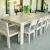 Juego de comedor Denali 2,4m para exterior en madera clara con ocho sillas y un banco, decorado con un florero con hojas verdes.