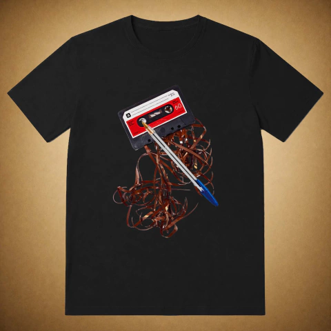 Camiseta preta unissex com estampa centralzada de uma fita k7 com rotulo vermelho e branco desenrolada e cantea bic com tampa azul por cima.
A estampa é uma foto e foi a primeira da Nas Antigas