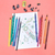 Imagem de um conjunto de lápis de colorir ecológicos de 12 cores ao lado de uma folha com desenho de foguete e planetas, sobre fundo rosa.