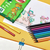 Conjunto de lápis de colorir ecológicos em várias cores, com um desenho infantil em papel ao lado.