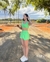 Mulher posando ao ar livre, vestindo um conjunto verde com short e top, em um cenário natural com árvores ao fundo.