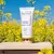 Frasco do hidratante Dream by Coconut da Brand Collection em fundo de flores amarelas sob céu azul