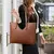 Bolsa shopper marrom usada no ombro por modelo, ideal para look urbano e elegante.