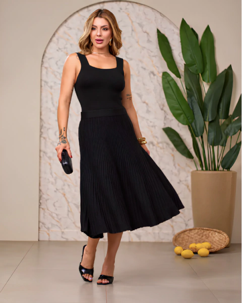 Mulher usando saia preta em modal com blusa regata preta, sandálias pretas e segurando uma pequena bolsa preta.