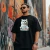 Homem usando camiseta preta com estampa de gato branco segurando placa com texto engraçado "Não sou Uber, mas me chama que eu te pego!"