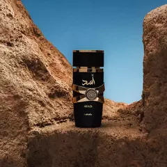 alt="Perfume Asad de Lattafa en ambientación desértica con fondo de cielo azul, estilo árabe sofisticado"