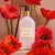 Botella de crema para manos y cuerpo Amapola & Vainilla de Essense & Co con flores rojas de amapola y una vaina de vainilla