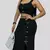 Mujer luciendo un conjunto de falda y crop top negro en tela suplex, con botones decorativos y abertura lateral, posando en un espacio interior moderno. El conjunto resalta su figura y combina estilo, comodidad y elegancia casual.