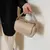 Bolsa feminina de ombro crossbody bege clara com fecho dourado sendo segurada por uma mão feminina