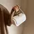 Bolsa feminina de ombro crossbody branca sendo segurada por uma mão.