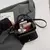 Bolsa feminina de ombro crossbody preta aberta mostrando interior com celular, carteira pequena e itens de maquiagem, sobre um blazer cinza.
