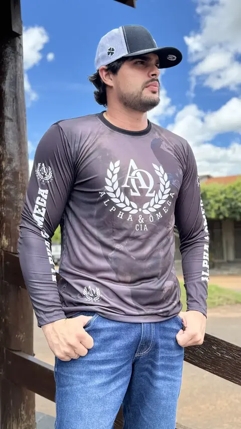 Homem vestindo camiseta Dry Fit Alpha & Ômega de manga longa cinza escuro com estampa branca e boné preto com branco em ambiente externo
