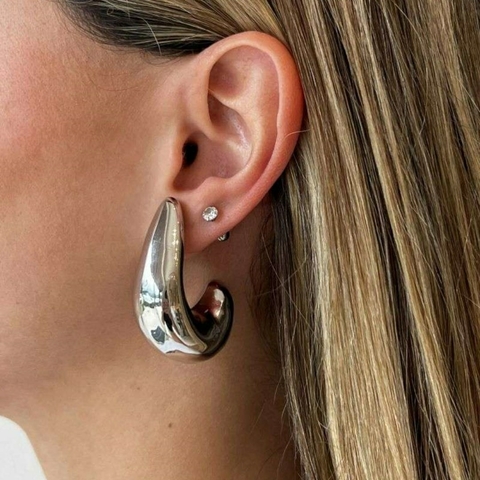 Brinco grande em formato de meia-lua com acabamento prateado usado em orelha feminina