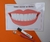 Imagem de um cartaz com um sorriso mostrando dentes brancos e saudáveis, acompanhado de uma escova de dentes e um marcador, com a frase "Vamos escovar os dentes!"