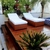 Conjunto de duas espreguiçadeiras Jardins em fibra sintética marrom com estofado branco, posicionadas em deck de madeira ao lado de piscina e plantas tropicais