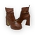 Bota feminina marrom em couro com plataforma e salto alto de 10cm, detalhe de fivela dourada e acabamento elegante