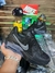 Tênis Nike Air Max Excee preto e cinza em exposição sobre superfície de vidro, com caixa Nike vermelha ao fundo e acessórios como boné preto com logo NY, relógio dourado e óculos esportivos.