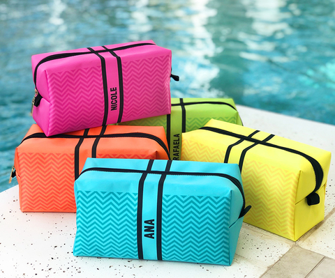 Kit com 5 necessaires personalizadas em cores neon, dispostas à beira de uma piscina. As bolsas são feitas de tecido, cada uma em uma cor vibrante diferente, ideais para praia ou presentes.