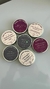 Sete velas aromatizadas em latas redondas com rótulos personalizados contendo frases engraçadas e descrições de aromas, dispostas sobre superfície branca.