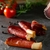 Bresaola maturada artesanal fatiada disposta sobre superfície escura com tomates e ervas ao fundo