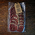 Pacote com fatias de bresaola maturada do Kit Sanduba de Mestre sobre superfície de madeira