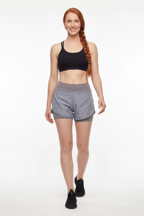 Mulher sorridente com cabelo ruivo trançado usando shorts duplo cinza e top esportivo preto