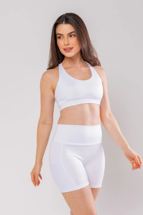 Mulher vestindo top esportivo branco e bermuda branca justa com bolso lateral em detalhe carmel