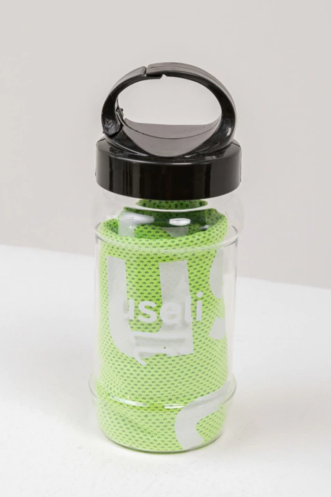 Kit Garrafa transparente com tampa preta contendo toalha verde enrolada, com a marca Useli visível na garrafa