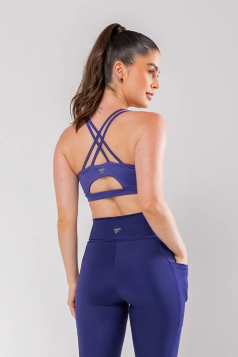 Mulher vestindo top esportivo azul com alças cruzadas nas costas e calça legging azul com bolso lateral
