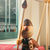 Boneco de madeira Hugo segurando um escudo e uma lança, com detalhes em diferentes tons de madeira, posicionado sobre um livro vermelho próximo a uma janela