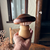 Objeto artesanal em forma de cogumelo feito de madeira nas mãos de uma pessoa, com tampo escuro e base clara