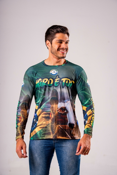 Homem sorridente vestindo camisa masculina de manga longa com estampa temática agro, incluindo elementos de agricultura e pecuária