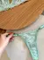 Calcinha de renda verde clara com detalhes delicados e alças finas em forma de coração segurada à mão feminina