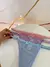 Três calcinhas Vanessa em tule com regulagem em cores azul, lilás e rosa, dispostas sobre uma superfície branca