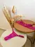 Conjunto de lingerie sensual rosa em renda com sutiã e calcinha, exibido sobre mesas redondas ao lado de arranjo de flores secas decorativas