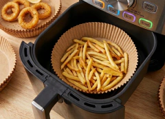 Molde de papel descartable con papas fritas dentro de la canasta de una freidora de aire