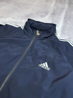 Campera rompevientos Adidas azul marino con cierre frontal y logo blanco bordado en el pecho, talle M