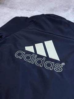 Campera rompevientos Adidas negra con logo grande en blanco sobre el respaldo