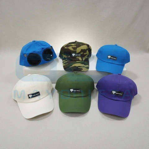 Seis gorras de diferentes colores, una azul con gafas integradas en el frente, camuflada, azul lisa, blanca, verde y morada, todas con un pequeño parche negro con texto blanco