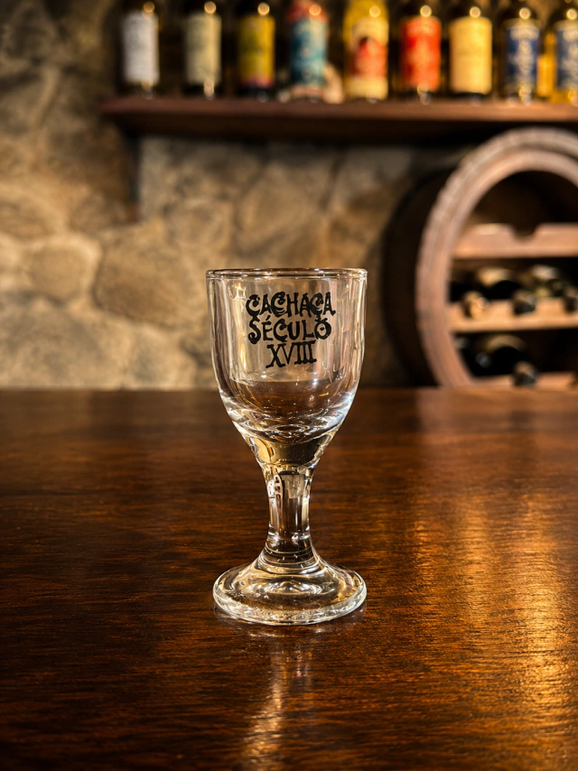Mini ta&ccedil;a com o logo da Cacha&ccedil;a S&eacute;culo XVIII sobre balc&atilde;o de madeira